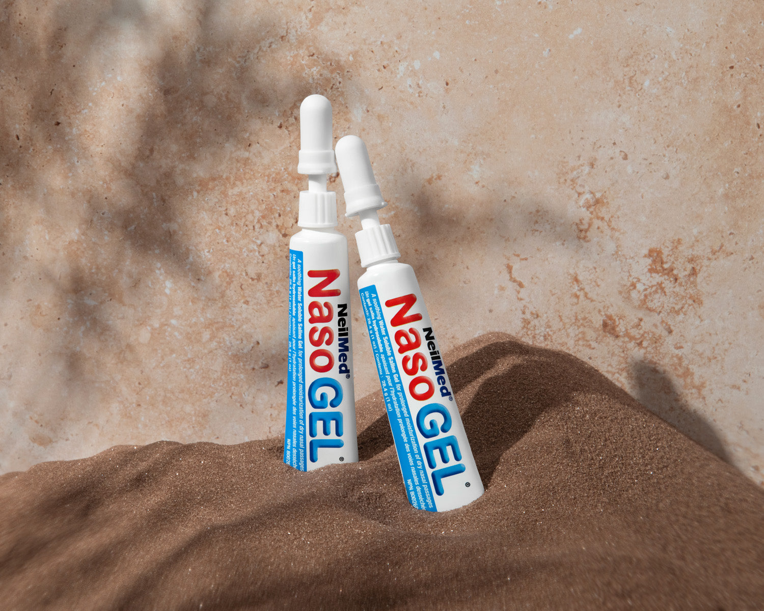 Two tubes of NasoGel on a sandy surface with a blurred natural background