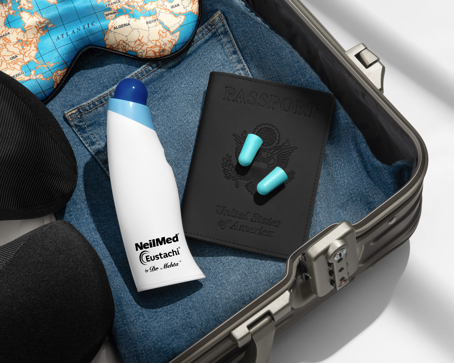 Travel accessories including a NeilMed Eustachy bottle, black case with earplugs, and a map on denim fabric.