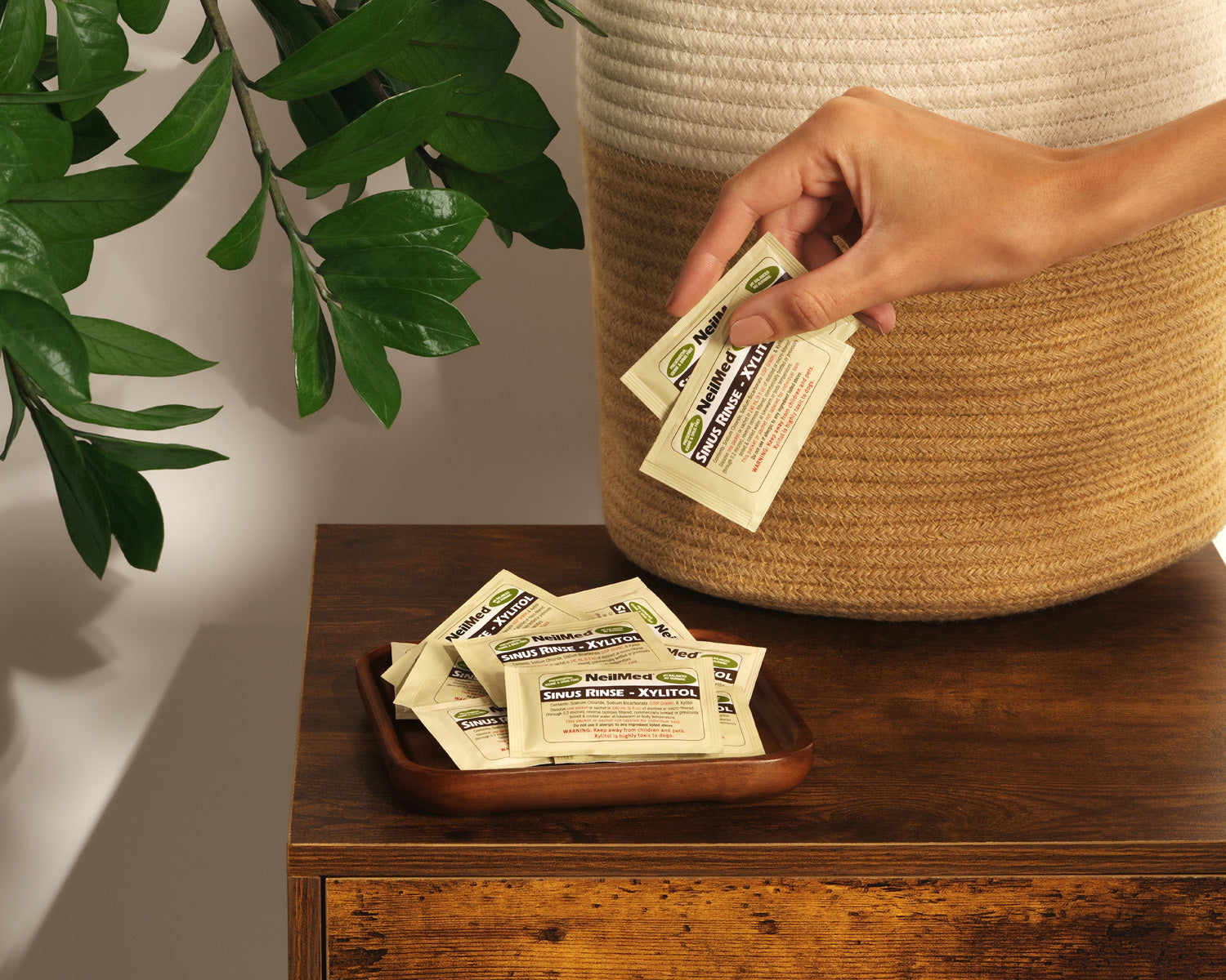 Hand reaching for packets of Sweet Leaf tea on a wooden surface with a plant in the background