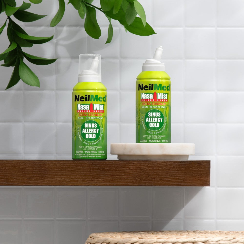 Two green bottles of NeilMed sinus allergy cold relief products on a wooden shelf with a plant in the background.