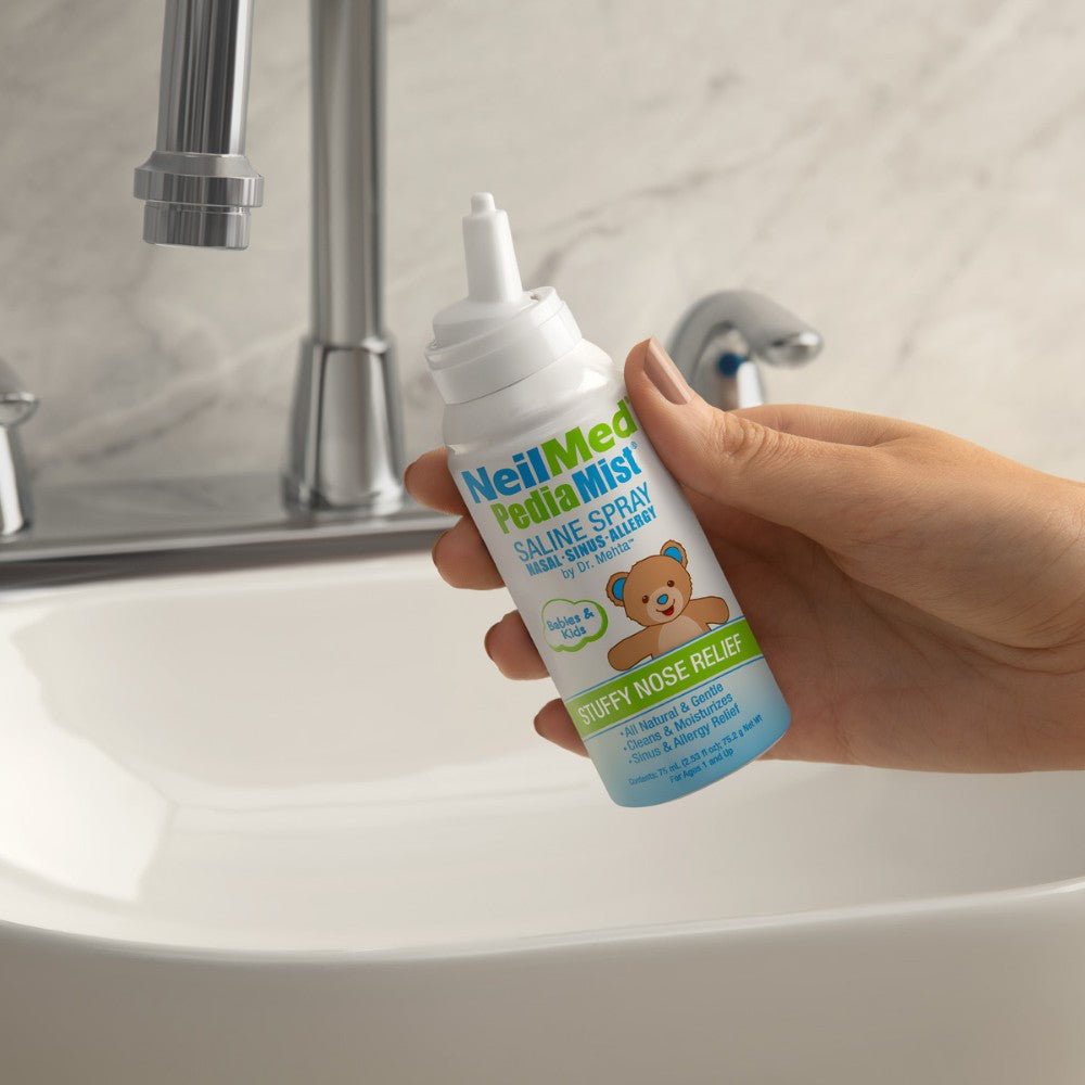 Hand holding a NeilMed PediaMist bottle in front of a sink.