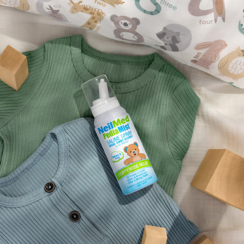 NeilMed Pediatric Saline Spray on a child's outfit with blocks and a patterned pillow in the background